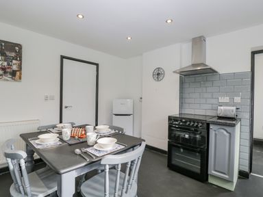 A kitchen with a dining table set for four a black stove a toaster a small white fridge and grey chairs at Pool House The Narth near Trellech