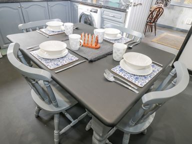 A kitchen dining table set for four with bowls, mugs, cutlery, and blue floral placemats at Pool House The Narth near Trellech