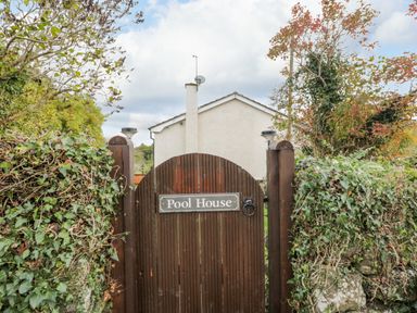 A wooden gate with pool house sign surrounded by greenery and a white house in the background at The Narth near Trellech