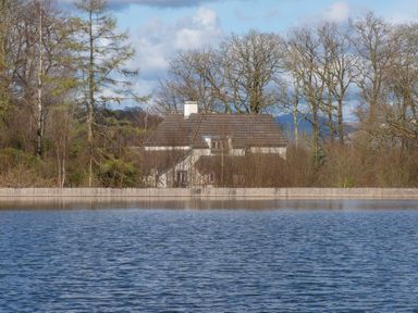 A house behind trees next to a water body at Keepers Cottage Hawkshead