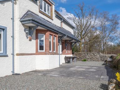 Exterior of a house with gravel and paved patio area next to a stone wall with bare trees in the background at Keepers Cottage in Hawkshead