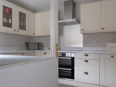 A kitchen with white cabinets a microwave oven a stove with a stainless steel hood and a bread box at Keepers Cottage in Hawkshead