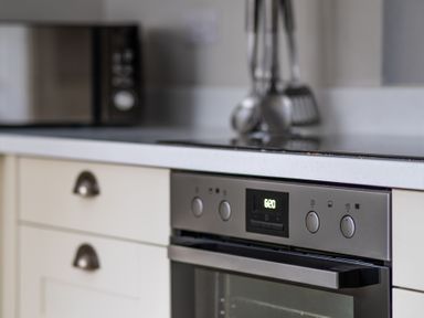 A kitchen countertop with a built-in oven and microwave with utensils on the counter at Keepers Cottage in Hawkshead