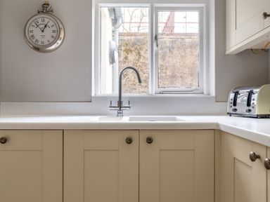 A kitchen with a sink under a window a wall clock and a toaster on the counter at Keepers Cottage in Hawkshead