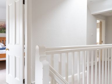 A hallway with white wooden railing leading to two open doors with one bedroom visible at Keepers Cottage Hawkshead