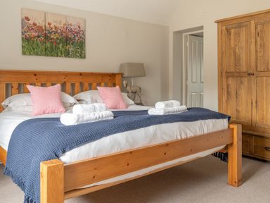A bedroom with a wooden bed with pink pillows white towels and a blue blanket a wooden wardrobe and a floral painting at Keepers Cottage in Hawkshead