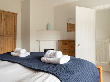 A bedroom with a bed covered by a dark blue blanket and two sets of folded white towels on top at Keepers Cottage in Hawkshead