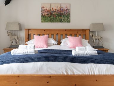 A bedroom with a wooden bed and pink pillows with towels on a blue throw at Keepers Cottage in Hawkshead