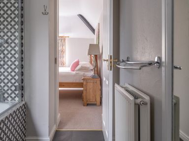 A view from a bathroom into a bedroom with a wooden bedside table and lamp at Keepers Cottage in Hawkshead