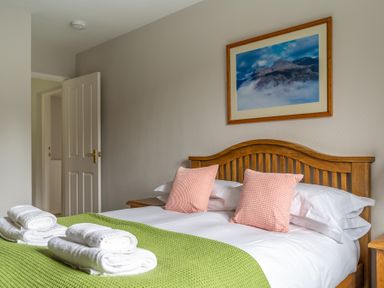 A bedroom with a wooden bed with pink cushions white towels and a green throw at Keepers Cottage in Hawkshead