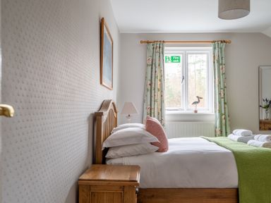 A bedroom with a wooden bed and side table a window with floral curtains and a green blanket on the bed at Keepers Cottage in Hawkshead