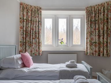 A bedroom with two single beds white linens floral curtains and a vase with flowers at Keepers Cottage in Hawkshead