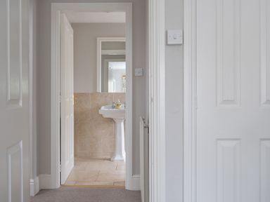 A hallway leading to a bathroom with a pedestal sink and tiled walls and floor at Keepers Cottage in Hawkshead
