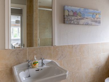 A bathroom with a white sink and soap dispenser a mirror reflecting a bedroom and a painting on the wall at Keepers Cottage in Hawkshead