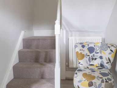 A carpeted staircase next to a floral patterned upholstered chair and a radiator at Keepers Cottage in Hawkshead