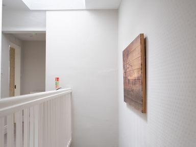 A hallway with white walls and railing with a wooden artwork on the wall at Keepers Cottage in Hawkshead