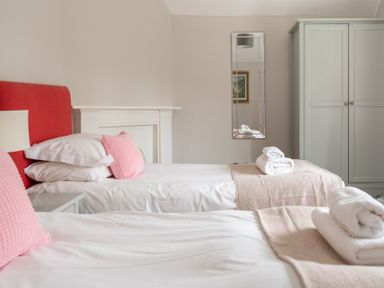 A bedroom with two single beds with pink cushions and folded towels a mirror and a wardrobe at Keepers Cottage in Hawkshead