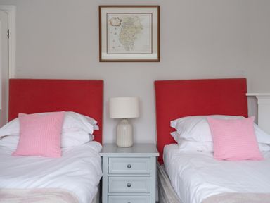 A bedroom with two single beds with red headboards and pink pillows a gray bedside table with a lamp and a framed map on the wall at Keepers Cottage Hawkshead