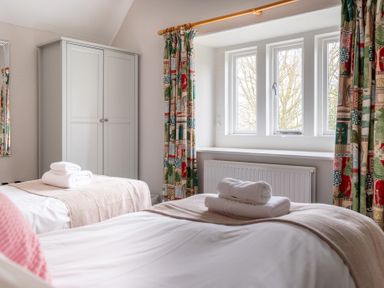 A bedroom with two single beds with folded towels on them a wardrobe and a window with patterned curtains at Keepers Cottage Hawkshead