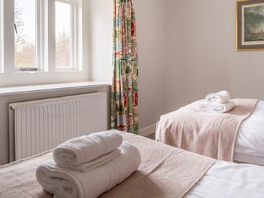 A bedroom with two single beds with folded towels near a window with patterned curtains at Keepers Cottage in Hawkshead