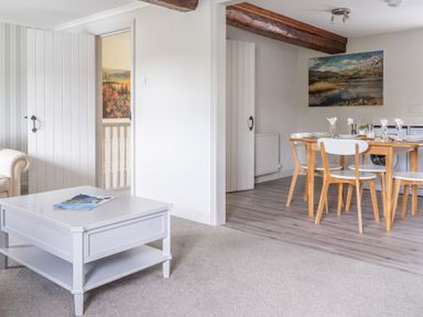 A living room with a white coffee table and part of a beige sofa and a dining area with a wooden table and white chairs at Grassholme in Hawkshead