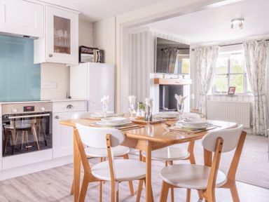 A dining table set for four in a kitchen adjoining a living room with a mounted television at Grassholme in Hawkshead