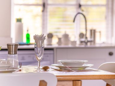 A kitchen table set with plates spoons a glass with napkins and a salt grinder at Grassholme in Hawkshead