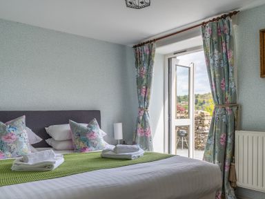 A bedroom with a bed with pillows and towels next to an open door with floral curtains at Grassholme Hawkshead