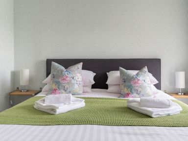 A bed with pillows and towels on a green blanket with lamps on wooden shelves at Grassholme in Hawkshead