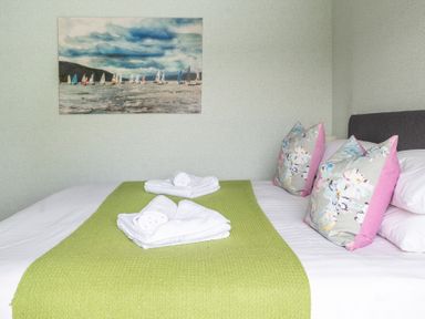 A bed with white sheets green runner folded towels and floral pillows with a painting of sailboats on the wall at Grassholme in Hawkshead