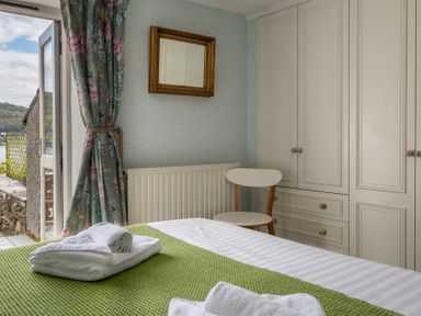 A bedroom with a bed covered in green blanket and white towels near a floral curtain and a white chair at Grassholme in Hawkshead