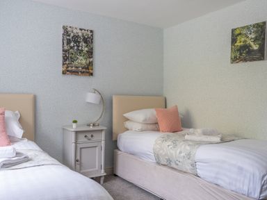 A bedroom with two single beds a bedside table with a lamp and paintings on the walls at Grassholme in Hawkshead