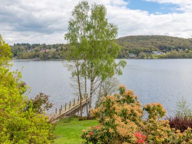 A lake with a wooden jetty and trees in the foreground at Grassholme in Hawkshead