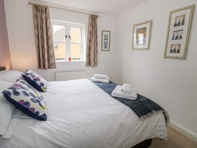 A bedroom with a double bed with white bedding blue patterned pillows and folded towels on a blue throw at Rosemead in Moreton-In-Marsh
