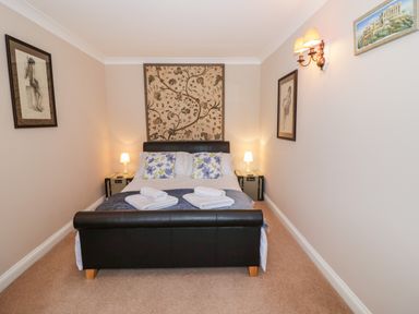 A bedroom with a double bed two bedside tables with lamps and framed pictures on the walls at Rosemead in Moreton-In-Marsh