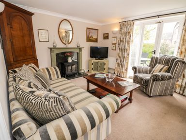 A living room with striped sofa and armchair a wooden coffee table and fireplace at Rosemead in Moreton-In-Marsh