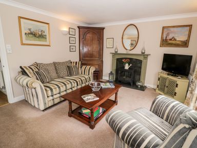 A living room with striped sofa and armchair wooden coffee table fireplace and television at Rosemead in Moreton-In-Marsh