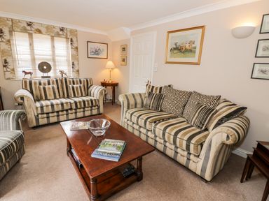 A living room with striped sofas a wooden coffee table and framed artwork on the walls at Rosemead in Moreton-In-Marsh