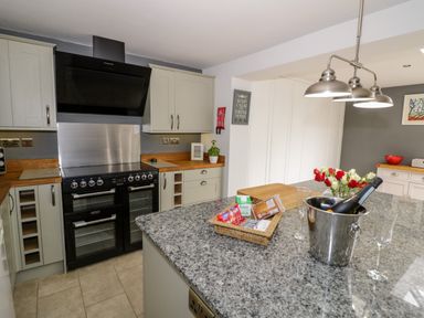 A kitchen with a black stove, grey cabinets, a granite island with a champagne bucket and flowers at Rosemead in Moreton-In-Marsh