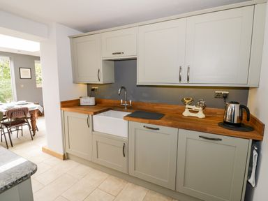 A kitchen with gray cabinets wooden countertops a white farmhouse sink a kettle and a scale at Rosemead in Moreton-In-Marsh