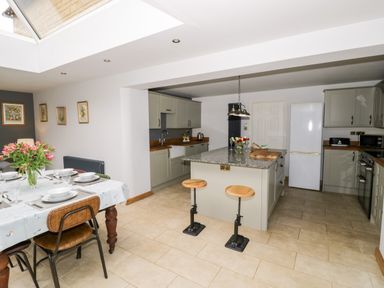 A kitchen with an island and two stools next to a dining table with chairs at Rosemead in Moreton-In-Marsh