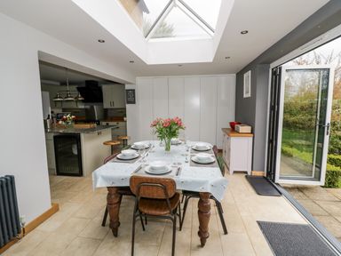 A dining area with a table set for six under a skylight next to an open glass door leading outside at Rosemead in Moreton-In-Marsh