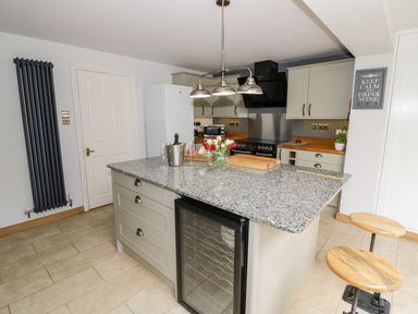 A kitchen with an island and bar stools a refrigerator and oven with a light fixture above at Rosemead in Moreton-In-Marsh