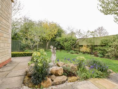 A garden with a stone statue surrounded by plants and flowers near a paved patio at Rosemead in Moreton-In-Marsh
