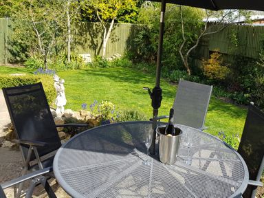 A backyard with a round metal table set with a bottle in an ice bucket and three glasses surrounded by outdoor chairs at Rosemead in Moreton-In-Marsh