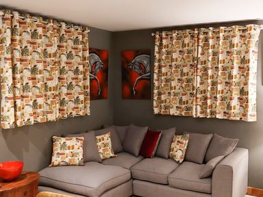 A living room with a gray sectional sofa patterned curtains horse paintings and a wooden side table with a red bowl at Rosemead in Moreton-In-Marsh