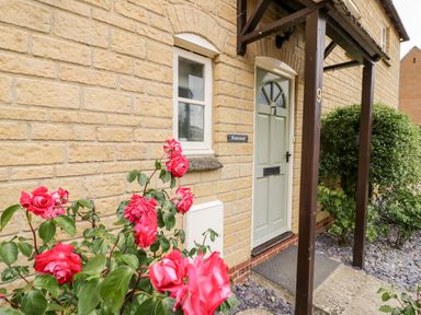 Front door with roses and shrubs near a stone wall at Rosemead in Moreton-In-Marsh