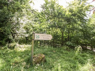 A wooden signpost in grassy area with trees behind pointing to Snowshill Manor