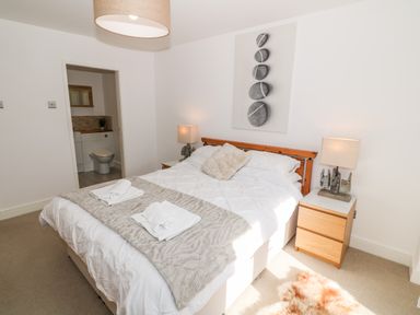 A bedroom with a double bed two bedside tables with lamps and an open door showing a bathroom at Bay View in Trearddur Bay