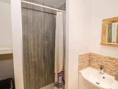 A bathroom with a shower area with a curtain and a sink with a mirror above and stone tile backsplash at Bay View in Trearddur Bay